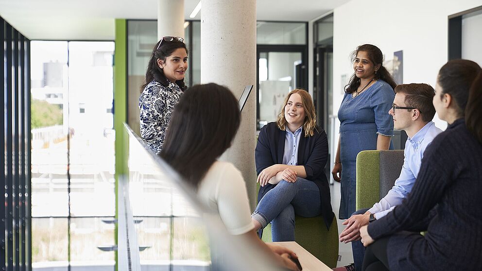 Fünf Frauen und ein Mann sitzen bzw. stehen zusammen und unterhalten sich miteinander.
