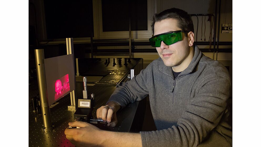 Foto (Universität Paderborn): Doktorand Holger Mühlenbernd demonstriert im Optiklabor die Erzeugung einer holografischen Abbildung.