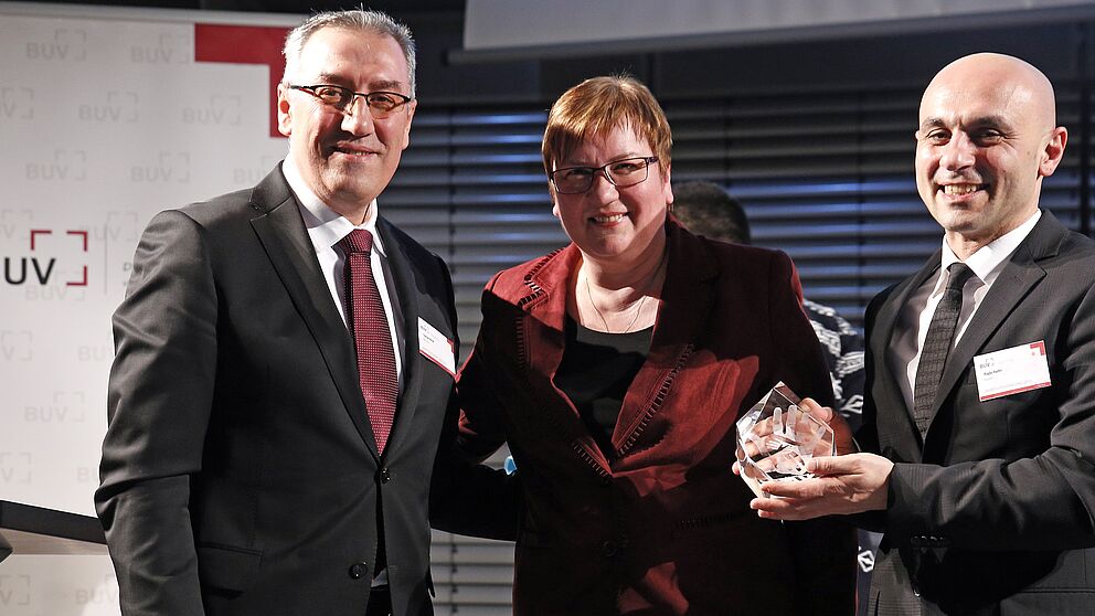Foto (Raynet GmbH), v. li.: Der Präsident des BUV, Osman Kimil, und die Parlamentarische Staatssekretärin beim Bundesminister für Wirtschaft und Energie, Iris Gleicke, gratulieren Ragip Aydin.