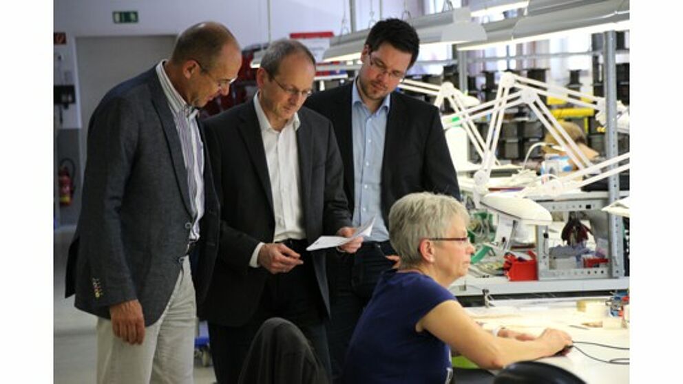 Foto: Wolfgang Kaiser (Friedr. Freek GmbH, links) zeigt Prof. Dr. Niclas Schaper und Projektmitarbeiter Julian Decius (jeweils Universität Paderborn) den Einsatzort der im Projekt StraKosphere konzipierten Kompetenzmanagementtabelle.
