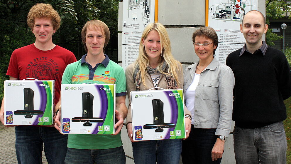 Foto (Uni Paderborn, Patrick Kleibold): (v. r.) Tobias Oetterer und Dr. Gudrun Oevel (beide vom IMT) überreichten den Studierenden Carina Doettger, Tim Gemmeke und Timo Schlüßler die XBoxen.