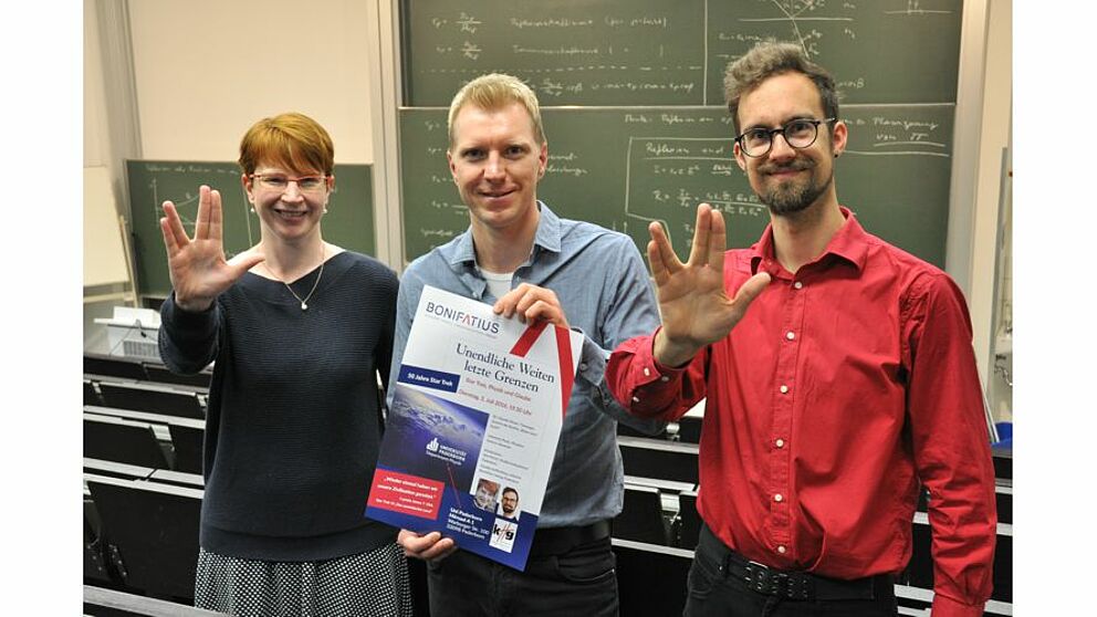 Foto (Claudia Auffenberg): Mit Trekkiegruß und Plakat (v. l.): Claudia Nieser, Studierendenpfarrer Nils Petrat und Johannes Pauly.