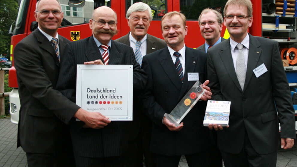 Foto (C.I.K.): Der Preisträger und die Festredner vor einem Feuerwehreinsatzwagen (v.l.n.r.): Prof Dr.-Ing. Detmar Zimmer (Dekan der Fakultät für Maschinenbau der Uni Paderborn), Jürgen Plato (Kanzler der Uni Paderborn), Heinz Paus (Bürgermeister der