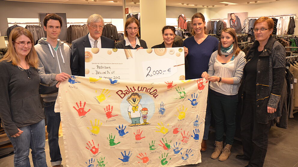 Foto (Stadt Paderborn): Bei der Spendenübergabe (v. l.): die Studierenden Julia Schlichting und Thomas Hüsgens, Bürgermeister Heinz Paus, Studentin Imke von Bargen, C&A-Filialleiterin Manuela Rodorff, die Studentinnen Maria Rockenfeller und Johanna Eic