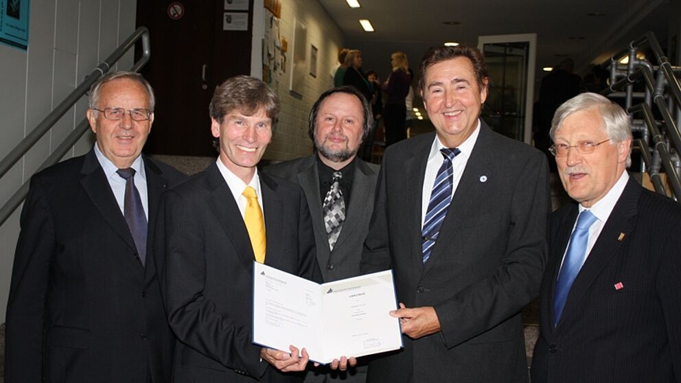 Foto (Tibor Werner Szolnoki, Universität Paderborn): Urkundenübergabe in Uni-Atmosphäre (v. li.): Altrektor Prof. Dr. Dr. h. c. Wolfgang Weber, Präsident Prof. Dr. Nikolaus Risch, Dekan Prof. Dr. Peter F. E. Sloane, Honorarprofessor Günther Goth und 