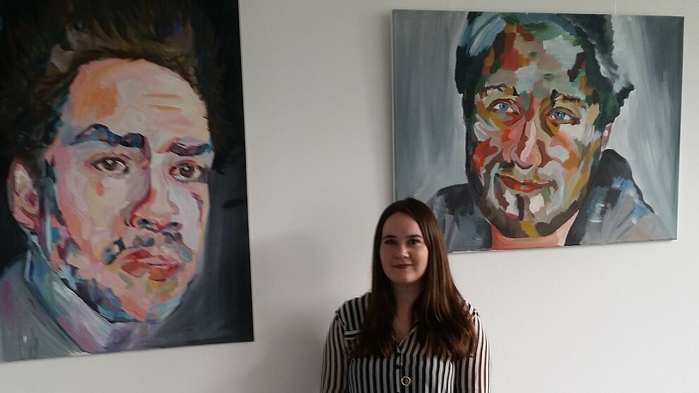 Foto: Katja Hardekopf vor einigen ihrer Porträtarbeiten auf der Ebene B2 der Uni Paderborn