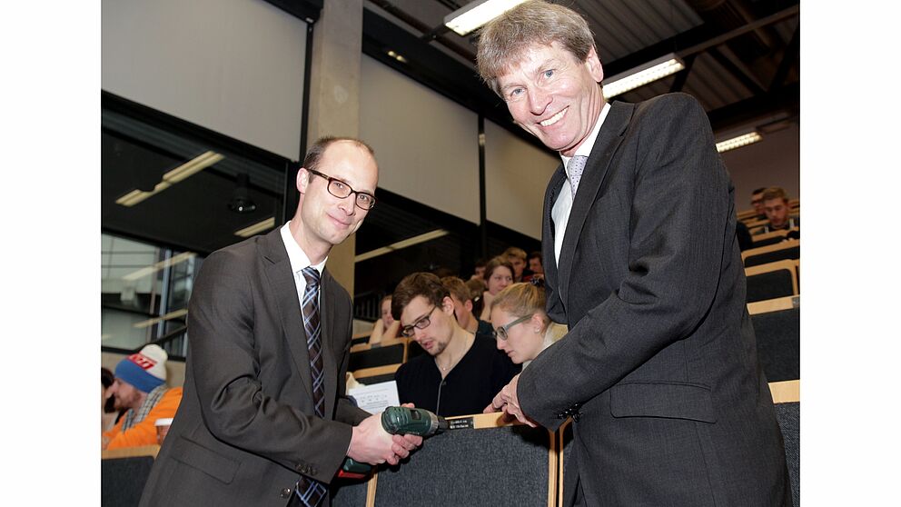 Foto (Universität Paderborn, Vanessa Dreibrodt): Dr. Oliver Middendorf, HLB Stückmann, (li.) bringt im Hörsaal die Plakette am „Leerstuhl“ an. Darüber freut sich Prof. Dr. Nikolaus Risch.