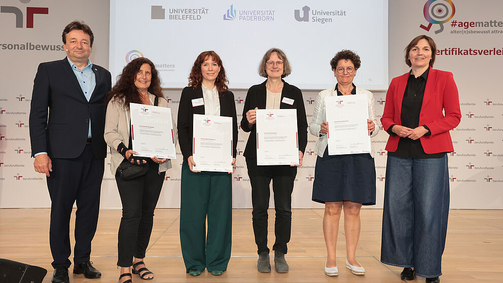 Ein Mann links und daneben fünf Frauen stehen in einer Reihe. Die vier Frauen in der Mitte halten Zertifikate in der Hand und halten diese in die Kamera.