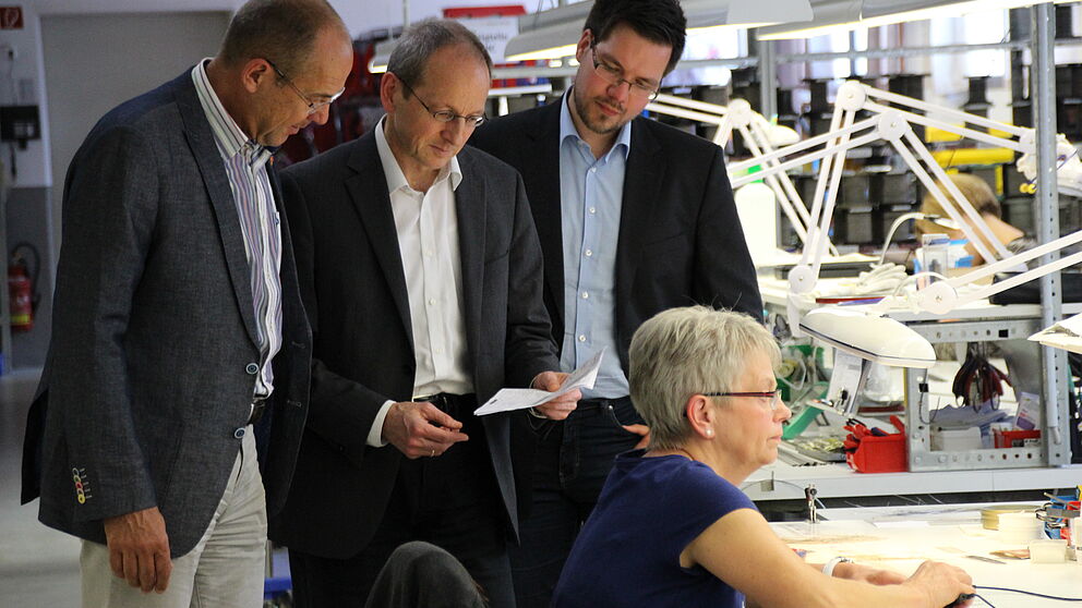 Foto: Wolfgang Kaiser (Friedr. Freek GmbH, links) zeigt Prof. Dr. Niclas Schaper und Projektmitarbeiter Julian Decius (jeweils Universität Paderborn) den Einsatzort der im Projekt StraKosphere konzipierten Kompetenzmanagementtabelle.