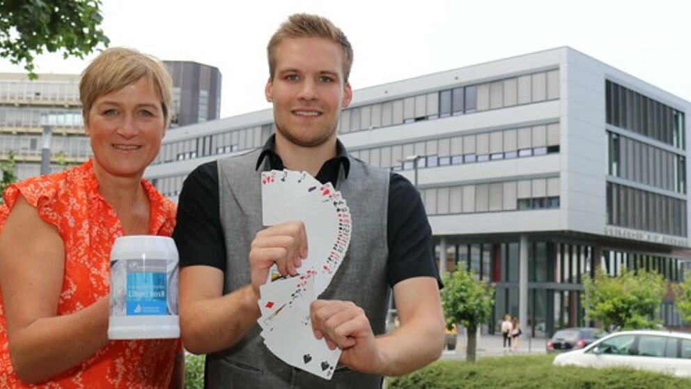 Foto (Universität Paderborn, Juliane Fröhling): Alexandra Dickhoff von Alumni Paderborn und Zauberer David Wedegärtner mit Kartentricks und Alumni-Krug beim kommenden Ehemaligen-Treffen der Universität.
