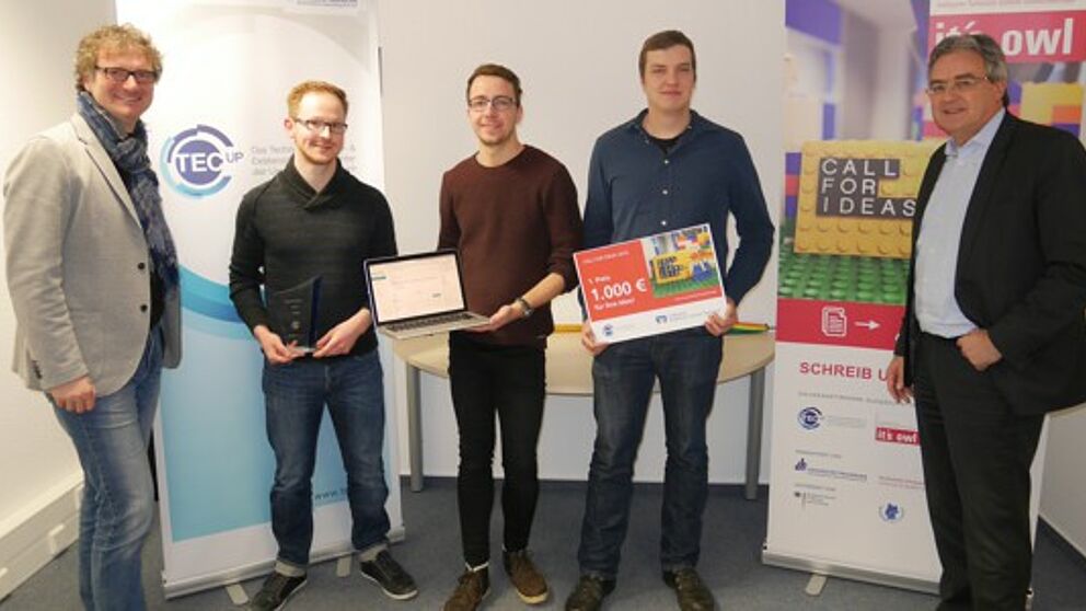 Foto (TecUP, Universität Paderborn): Zu Besuch bei dem Gewinnerteam 2016 Philipp Bednarek (2. v. l.), Christoph Bach (m.) und Marcel Hartmann (2. v. r.) – Rüdiger Kabst (l.) und Karl-Heinz Rawert (r.) freuen sich über die Fortschritte des jungen Star