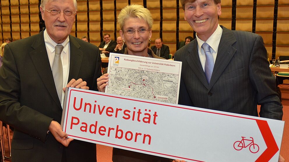 Hier geht's zur Universität Paderborn. Bürgermeister Heinz Paus (r.) und Claudia Warnecke, Technische Beigeordnete der Stadt Paderborn, überreichten Prof. Dr. Nikolaus Risch, Präsident der Universität Paderborn, symbolisch dieses Schild.