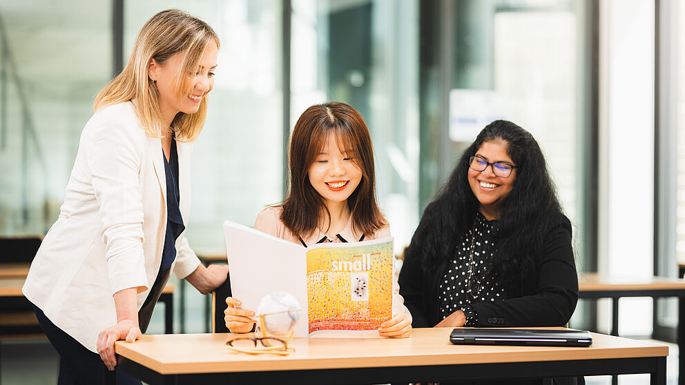 Three women sit at a table and look at a document