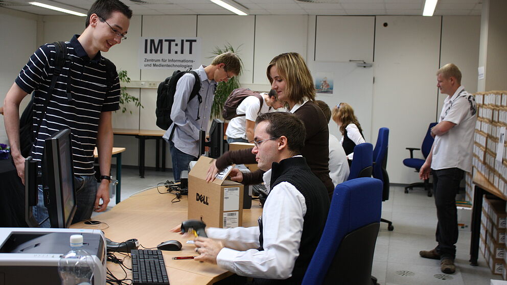 Foto (Frauke Döll): Auszubildende Jeannette Schopny und Sebastian Porombka, studentische Hilfskraft des IMT, statten die Erstsemester mit Netbooks und Informationen aus.