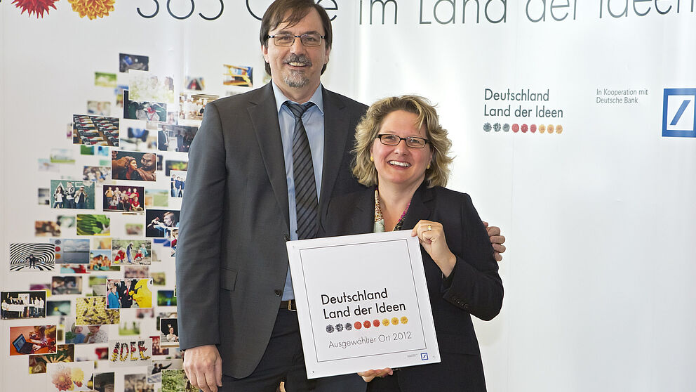 Abbildung (Quelle: „Deutschland – Land der Ideen/Uwe Völkner, Fotoagentur FOX“): Svenja Schulze, Ministerin für Innovation, Wissenschaft und Forschung des Landes Nordrhein-Westfalen, überreicht Prof. Dr. Gregor Engels, Vorstandsvorsitzender s-lab