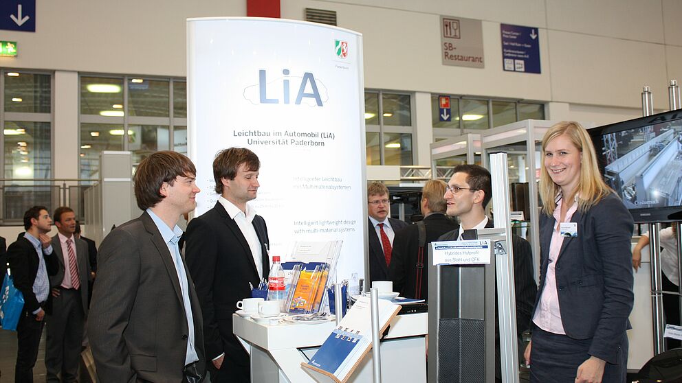 (Universität Paderborn, Fakultät für Maschinenbau): (v.l.n.r.) Zwei Fachbesucher der Messe im Gespräch mit Dipl.-Ing. Dipl.-Wirt.-Ing. Christian Lauter und Dipl.-Ing. Meike Frantz vom Lehrstuhl „Leichtbau im Automobil“.
