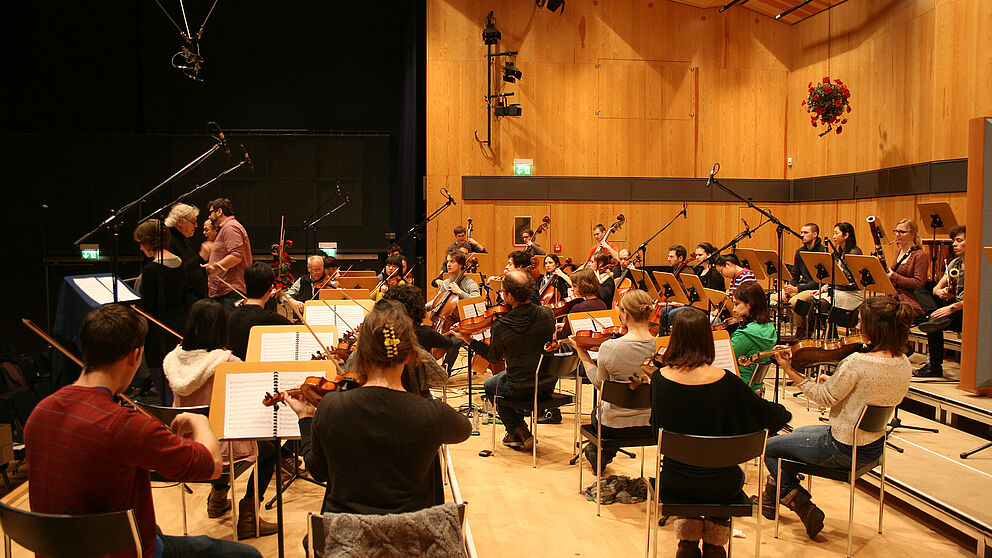 Abbildung: Tonaufnahmen in der Aula der Hochschule für Musik Detmold: Noch liegen gedruckte Noten auf den Pulten der Musiker. Bald können Dirigenten ihre Interpretation der Oper am Computer zusammenstellen und an die Notenständer ersetzende Tablets üb