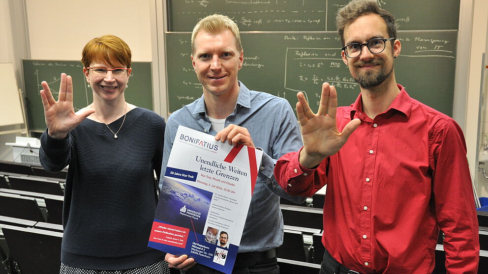 Foto (Claudia Auffenberg): Mit Trekkiegruß und Plakat (v. l.): Claudia Nieser, Studierendenpfarrer Nils Petrat und Johannes Pauly.