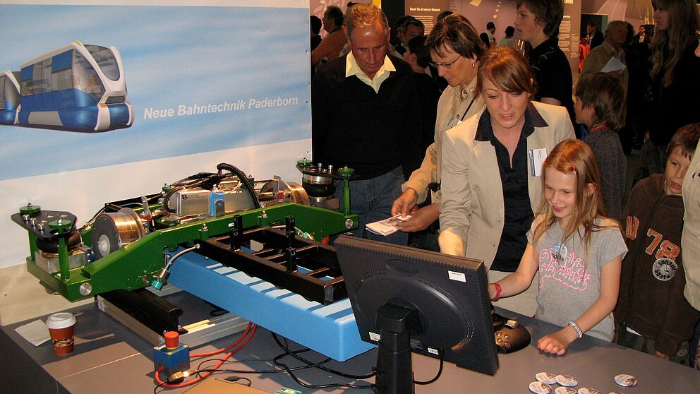 Foto (NBP): Diplom-Informatikerin Helene Waßmann (3. v. l.) von der NBP erklärt die Funktionsweise des sturzvariablen RailCab-Einzelachsfahrwerks.