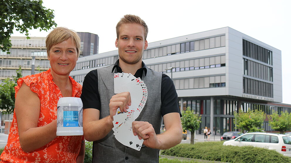 Foto (Universität Paderborn, Juliane Fröhling): Alexandra Dickhoff von Alumni Paderborn und Zauberer David Wedegärtner mit Kartentricks und Alumni-Krug beim kommenden Ehemaligen-Treffen der Universität.