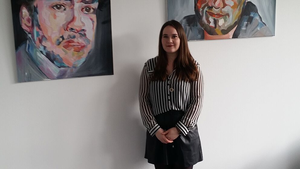 Foto: Katja Hardekopf vor einigen ihrer Porträtarbeiten auf der Ebene B2 der Uni Paderborn