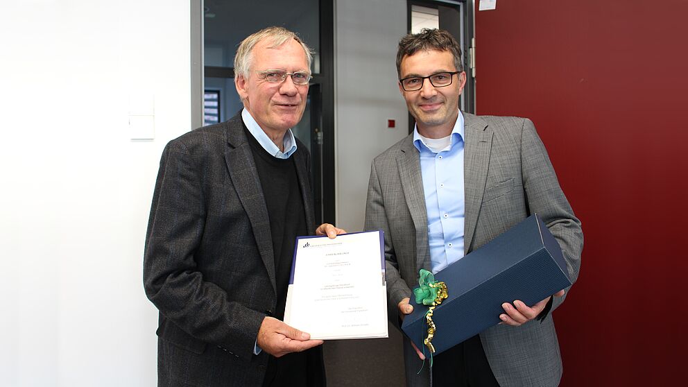 Foto (Universität Paderborn, Frauke Döll): Zusammen mit dem Jubilar Prof. Dr. Joachim Fischer (links) freut sich Prof. Dr. Martin Schneider, Dekan der Fakultät für Wirtschaftswissenschaften, im Kreise der Kolleginnen und Kollegen auf der Fakultätsrat